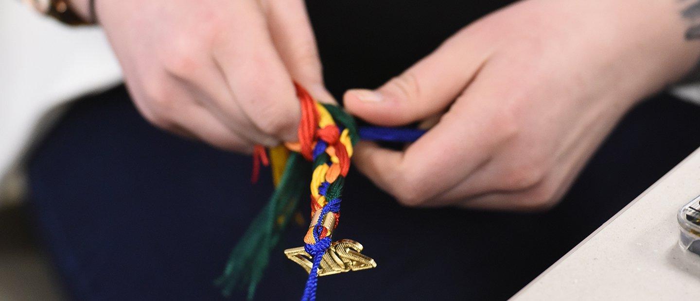hands braiding a rainbow colored graduation tassle