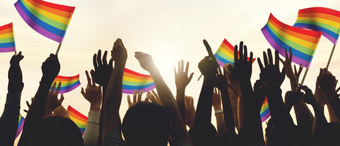 Hands pointing in the air and waving rainbow colored flags outside.